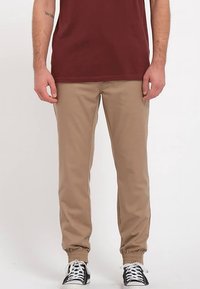 Beżowe spodnie dresowe z elastycznymi ściągaczami, wykonane z bawełnianej mieszanki tkanin, z bocznymi kieszeniami, zestawione z bordowym t-shirtem i czarnymi sportowymi butami na sznurówki.