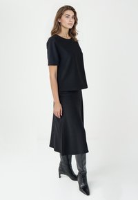 Czarny krótki top z krótkim rękawem i długa spódnica z miękkiego materiału, o luźnym kroju. Model nosi czarne kozaki do kolan. Minimalistyczny design.