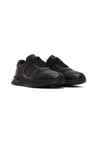 Un par de zapatillas deportivas de piel negra de corte bajo con cordones, suelas texturizadas y cuellos acolchados, sobre un fondo blanco.