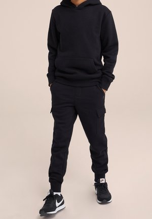 Felpa nera con tasca frontale, abbinata a pantaloni jogger coordinati con tasche cargo. Entrambi gli articoli hanno una texture liscia.