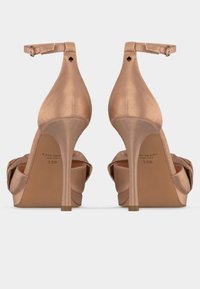 Ζευγάρι γυμνά σανδάλια από σατέν με ψηλό τακούνι, λουριά στον αστράγαλο, ανοιχτές μύτες και μικρό μαύρο λογότυπο σπαθί στη πίσω πλευρά κάθε τακουνιού.