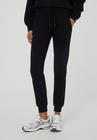 Pantaloni sportivi neri con polsini elastici, vita con cordoncino e tasche laterali, realizzati in tessuto morbido, abbinati a sneakers sportive argento.