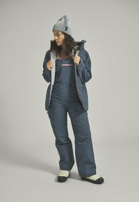 Navy waterproof jacket with gray accents and pink zipper, paired with matching overalls. Textured gray knit beanie and cream booties complete the outfit.