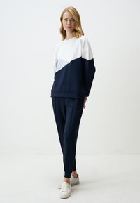 Marineblauwe en witte kleurblok sweatshirt met een ronde halslijn, gecombineerd met bijpassende getailleerde joggingbroeken. Glad materiaal, elastische manchetten en zijnaad.