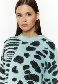 Mintgroene fuzzy trui met zwarte luipaardvlekken en strepen, voorzien van een ronde halslijn en een zachte textuur.