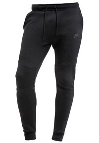 Pantalons de survêtement noirs en tissu doux, avec une coupe fuselée, une taille élastique à cordon de serrage et un logo discret sur la cuisse. Panneaux texturés pour le détail.