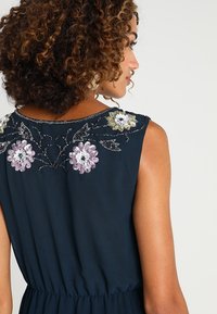 Granatowa, bezrękawnikowa sukienka z kwiatowym haftem na dekolcie w pastelowym różu i zieleni, z marszczoną talią i gładką fakturą.
