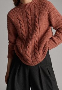 Sweter ze splotem w stonowanym kolorze terakoty, z wysokim okrągłym dekoltem, ściągaczami przy mankietach oraz szczegółowymi wzorami teksturowymi.