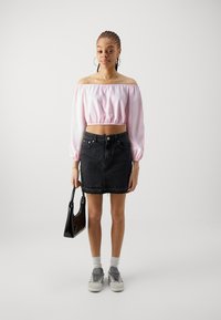 Off-shoulder rosa sateng crop-top med elastisk kant, kombinert med et svart denimskjørt og grå sneakers. Holder en svart håndveske.
