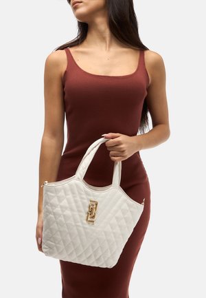 Sac fourre-tout matelassé blanc avec poignées doubles, détail de logo doré et forme structurée, doté d'une fermeture éclair et d'une texture lisse.