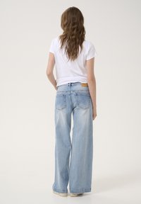Jeans a gamba larga di colore blu chiaro, realizzati in denim, con un lavaggio sbiadito. La vista posteriore mostra due tasche posteriori e un'etichetta in pelle beige nella vita.