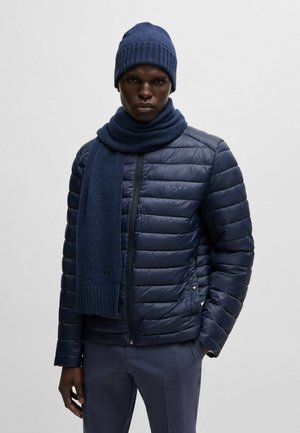 Navy puffy jacket with horizontal stitching, paired with a matching knit beanie and scarf. Smooth texture with a zip closure and logo detail.