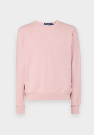 Vaaleanpunainen collegepaita, joka on valmistettu pehmeästä kankaasta. Siinä on pitkät hihat, pyöreä pääntie ja pieni kultainen logo rinnassa. Pinta on sileä.