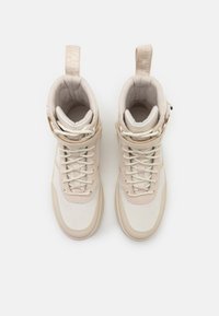 Sneakers beige alte con colli imbottiti, lacci frontali e linguette sul retro, viste dall'alto su uno sfondo bianco.
