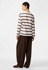 Valge ja pruuni triibuline pika varrukaga särk, mis on kombineeritud pruuni triibuliste laiade pükstega, millel on mugav lõige ja vabaaja disain.