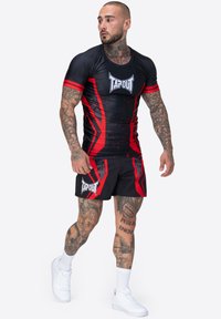 Conjunto atlético negro y rojo que presenta una camiseta ajustada de manga corta con un logo y un diseño gráfico audaz, combinada con pantalones cortos negros.