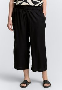 Pantalones cortos negros con una cintura elástica, fabricados en un tejido suave y con bolsillos laterales, combinados con sandalias negras tipo slide con un diseño trenzado.
