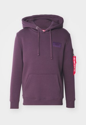 Sudadera morada hecha de un tejido suave, con un bolsillo frontal, cordones, un bolsillo lateral con cremallera y una etiqueta de tela colgando de la manga.