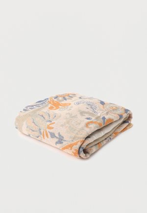 Tissu beige plié avec des motifs floraux et abstraits oranges et bleus sur un fond blanc uni.
