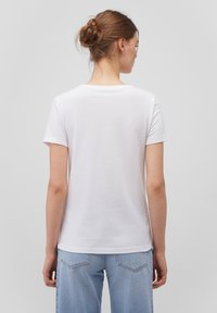 White cotton t-shirt with short sleeves, a rounded neckline, and a smooth texture, shown from the back, paired with light blue jeans.