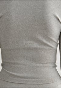 Top de manga larga gris confeccionado en una tela suave y elástica. Presenta un dobladillo acanalado y un logo sutil en la parte delantera. Diseño simple y ajustado.