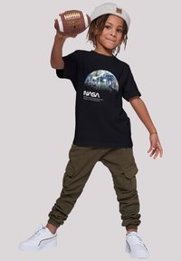 Black t-shirt with NASA logo and Earth graphic, olive green cargo pants, and white athletic shoes. Child holding a football.