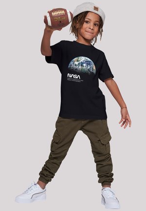 Black t-shirt with NASA logo and Earth graphic, olive green cargo pants, and white athletic shoes. Child holding a football.