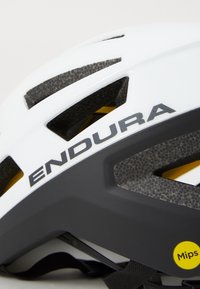 Weißer Fahrradhelm mit schwarzen Akzenten, der das "ENDURA"-Logo und einen "Mips"-Aufkleber zeigt, mit Belüftungsschlitzen und modernem Design.