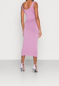 Robe midi ajustée rose avec un dos en scoop, en matériau extensible, et une longueur aux chevilles ; associée à des sandales à talons violettes et des talons blocs transparents.