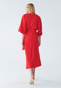 Rotes Midi-Kleid mit Fledermausärmeln, tailliertem Schnitt und seitlicher Bindung. Glattes Material und ein gerader Saum runden das Design ab.
