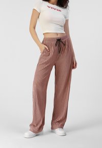 Růžové proužkované kalhoty s volným střihem, které mají černé vertikální pruhy, kapsy a černou šňůrku na stažení. V kombinaci s těsně přiléhajícím bílým tričkem s potiskem.