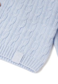 Světle modrý svetr s pleteným vzorem a žebrovanými manžetami, zdobený malou látkovou cedulkou s motivem králíka. Měkký, strukturovaný materiál.