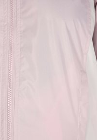Lys pink vindjakke med en glat, tekstureret overflade, der har en central lynlås og sidelommer, letvægtsstof og et minimalistisk design.