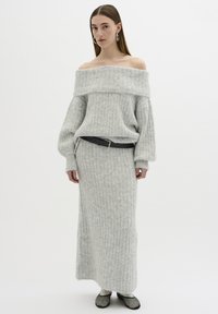 Compleu tricotat gri, format din două piese, cu un top off-the-shoulder și fustă lungă cu dungi. Prezintă manșete largi și un curea neagră. Material texturat.