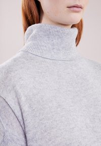 Ljusgrå turtlenecktröja i mjukt stickat tyg med ribbad krage och subtil textur. Närbild som betonar detaljer.