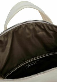 Interior de una bolsa, con una abertura con cremallera, exterior de tela beige y forro de satén marrón oscuro con una etiqueta visible.