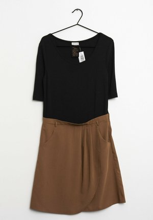 Schwarzes Oberteil mit rundem Ausschnitt und drei Viertelärmel, verbunden mit einem braunen, plissierten Rock mit Seitentaschen. Hängt an einem schwarzen Haken.