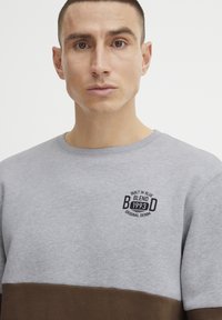 Gray and brown sweatshirt with a round neckline; features a logo patch in black text; soft texture; color-block design.
