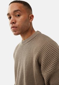 Strikket sweater i lys brun med et struktureret væv og en ribbet rund halsudskæring. Ærmerne er lidt løse for en afslappet pasform.
