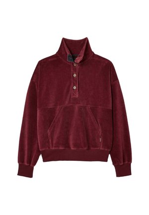 Burgundy corduroy pullover with a high collar, button details, and a front pocket, paired with brown checked wide-leg trousers and beige sneakers.