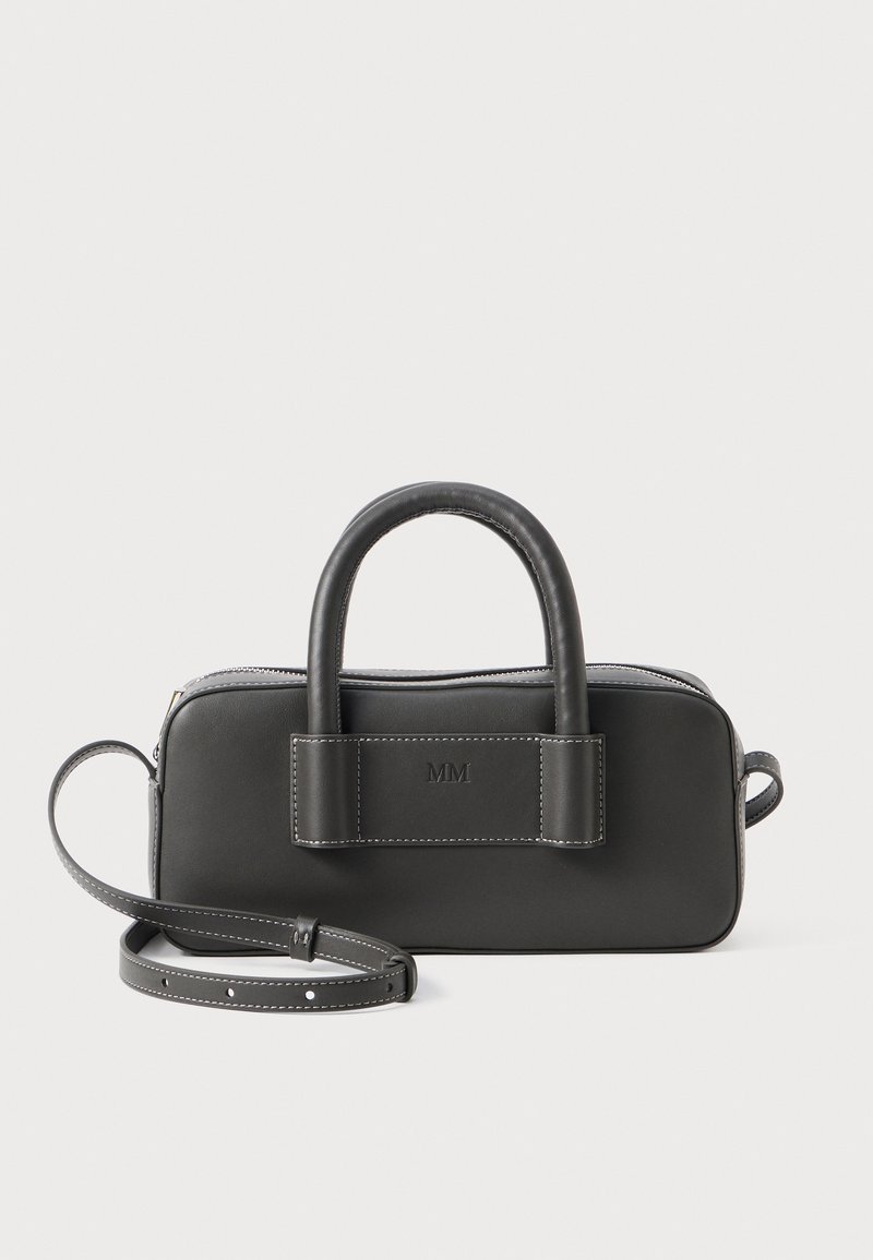 Svart lærveske med runde håndtak og justerbar stropp. Har glidelås-lukking og preget "MM"-logo på forsiden med hvite sømmer.