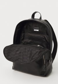 Zwarte rugzak met een gladde synthetische buitenkant, een voorvak met rits en een ruime binnenkant met een herhalend logopatroon.