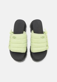 Par de sandalias de suela negra con tirantes acolchados de color verde neón que presentan el logo de UGG y cierres ajustables con cordón en un fondo blanco.