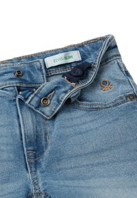 Jasnoniebieskie dżinsy o dopasowanym kroju. Posiadają zieloną metkę z napisem "ELVIS-SLIM", mosiężne guziki oraz subtelny haft.