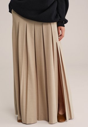 Beige long pleated skirt with a side slit, worn with a black sweater and brown closed-toe shoes, shown from waist to floor.