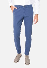 Chino in cotone blu con vestibilità slim, dotati di tasche frontali e chiusura a un solo bottone. Abbinate a stivali in suede grigio chiaro.