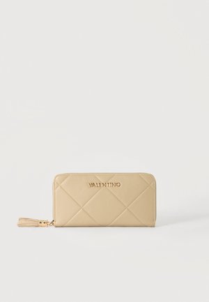 Portefeuille zippé en cuir matelassé beige Valentino avec logo doré et tirette à pompon sur fond blanc uni.