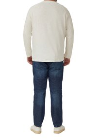 Koszula na długi rękaw w kremowym kolorze o luźnym kroju, zestawiona z ciemnoniebieskimi dżinsami i jasnymi trampkami. Proste detale wzornicze.