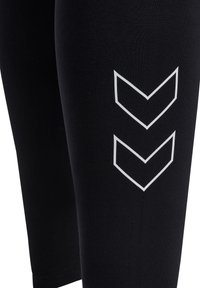 Schwarze Leggings aus einem dehnbaren Material mit einem weißen Chevron-Muster an der Seite. Das Design ist eng anliegend und hat eine glatte Textur.