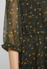 Vestido de color verde oscuro con estampado floral amarillo, tejido ligero, mangas transparentes con puños rizados y detalle de cintura elástica.
